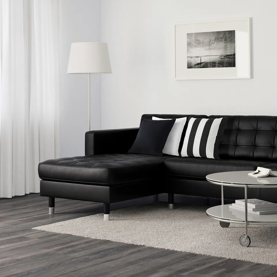 Modern living room with black l-shaped sofa, striped cushions, round coffee table, floor lamp, and wall art.