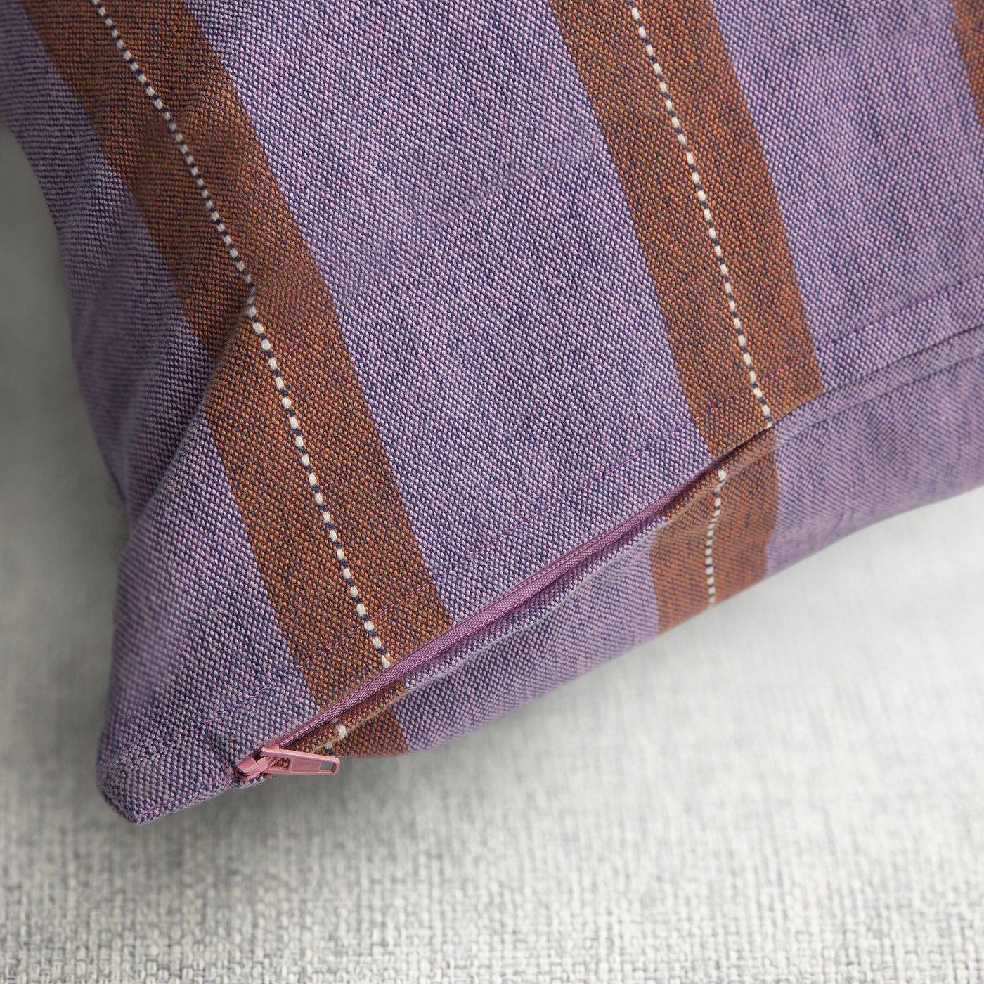 A striped pillowcase with zip closure, showcasing pink and orange stripes with blue base, handwoven with intricate patterns.