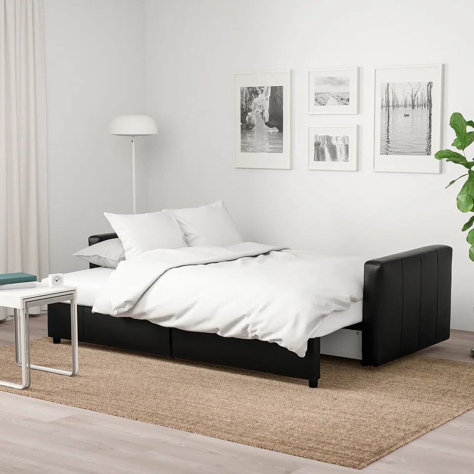 Black sleeper sofa with white bedding, photos, and lamp on rug.