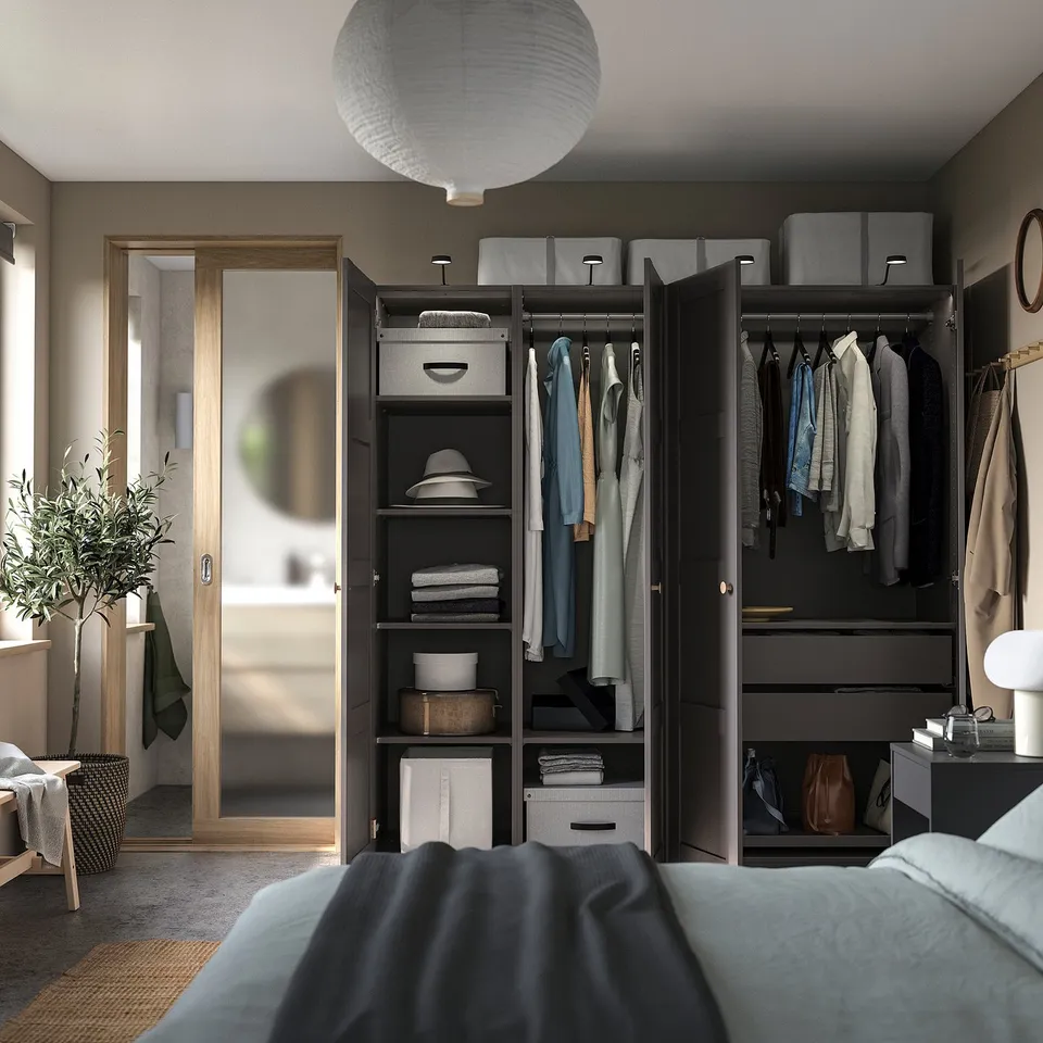 Modern bedroom with black PAX wardrobe, hanging clothes, shelves, and a large mirror. Grey bed and light fixture.