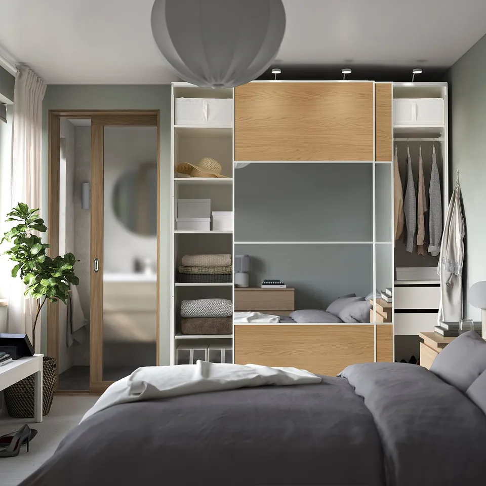 Modern bedroom with PAX wardrobe featuring sliding doors, open shelves, and hanging space, including a mirrored panel for added spaciousness.