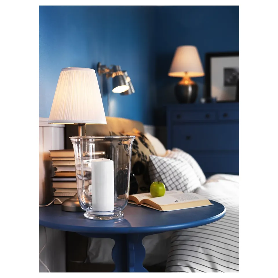 Bedroom table with blue table lamp, candle holder, books, and apple.