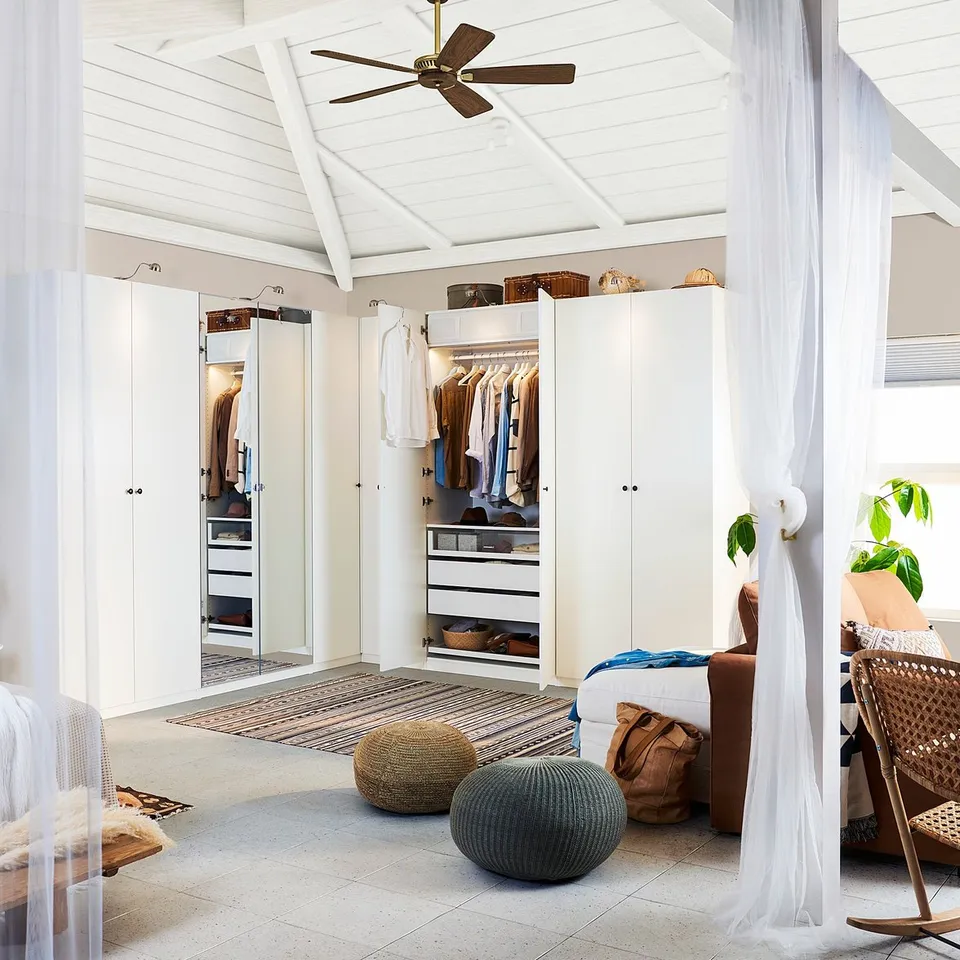 Bright, airy bedroom with white furniture, including FORSAND doors on pax wardrobes, a wicker chair, pouffes, and a striped rug underfoot.