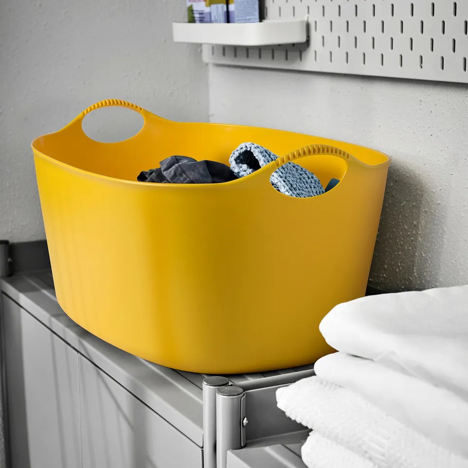 Bright yellow TORKIS laundry basket on shelf, larger than folded towels, made of flexible plastic with handles.