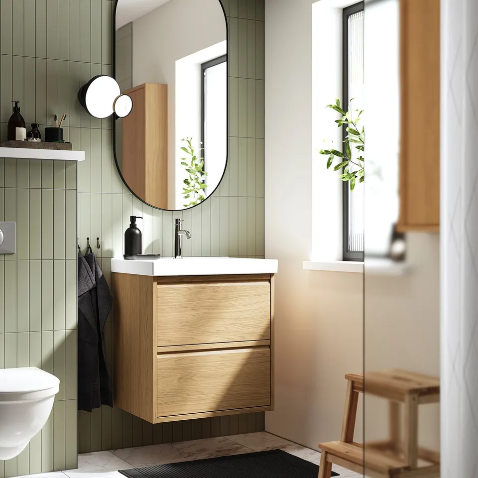 Modern bathroom with light wood vanity, green tiles, and large mirror.