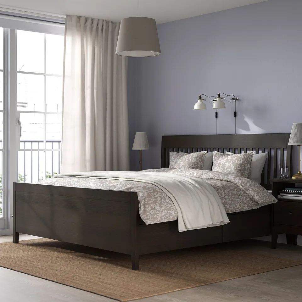 Modern bedroom with IDANÄS dark wood bed, storage, patterned bedding, wall lamps, grey walls, large window, beige rug.