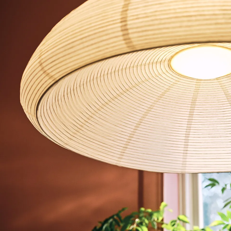 Close-up of a woven rice paper pendant lamp from IKEA, emitting a soft glow, attached to a steel and galvanised ceiling cup.