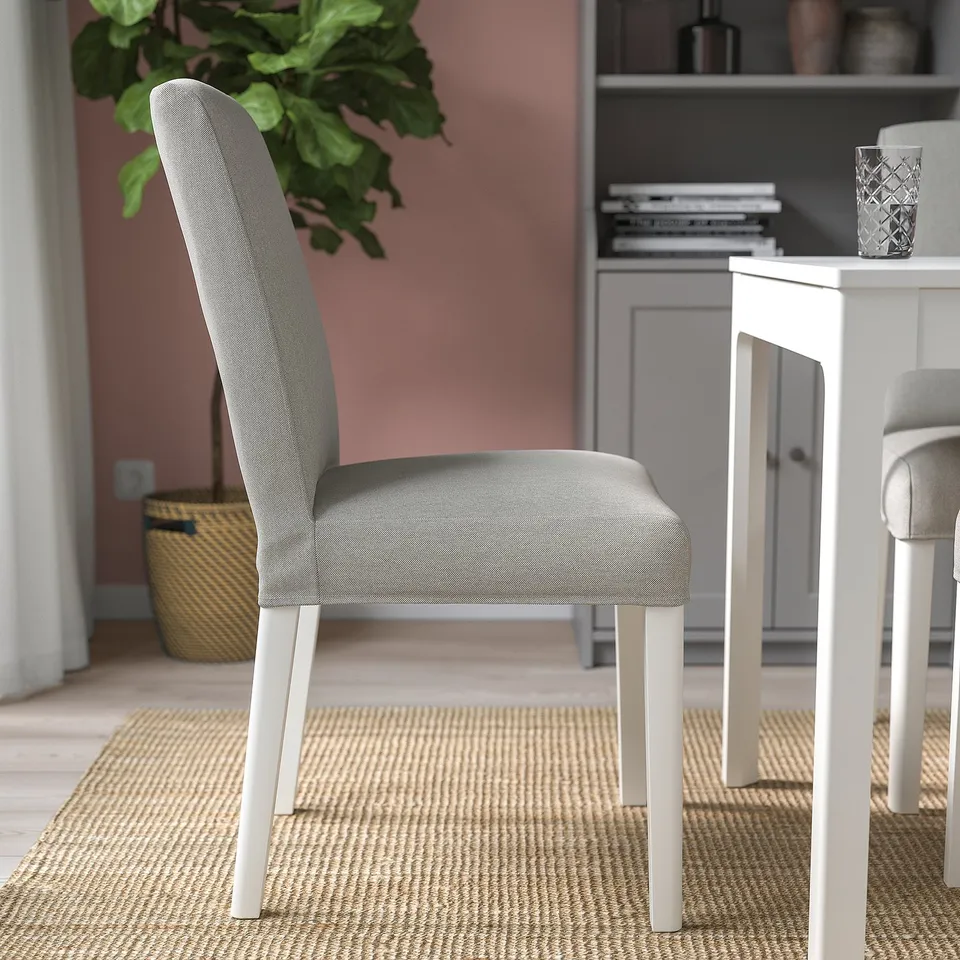 Modern dining setup with grey upholstered chair, white metal legs, on woven rug near table with glass vase.