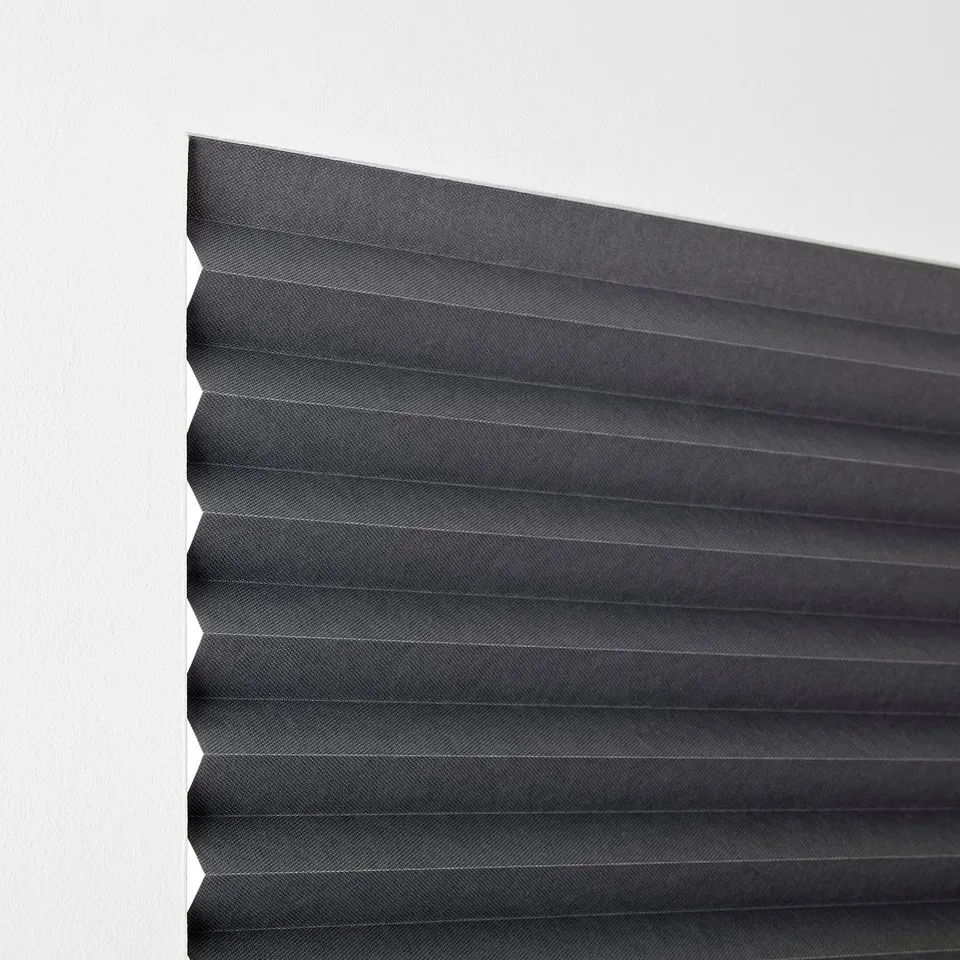 A grey block-out blind, partially folded, designed to darken rooms. It attaches easily without drilling and can be secured in place.
