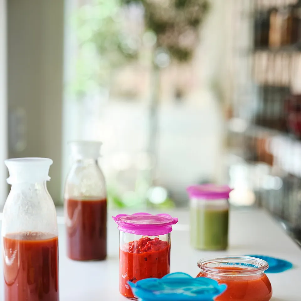 Kitchen counter with colourful jarred sauces & smoothies, cucumbers, spoon.