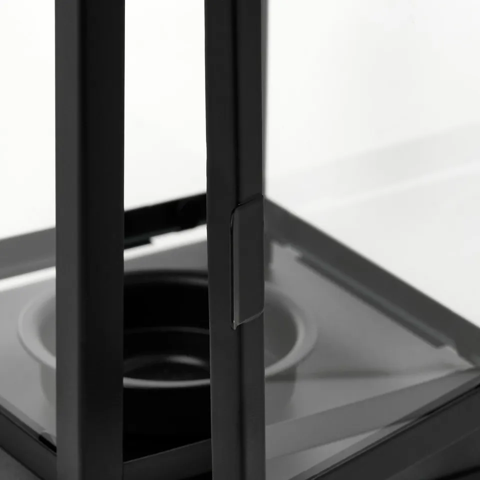 Black lantern with clear glass front, sturdy metal frame, and handle, photographed indoors.