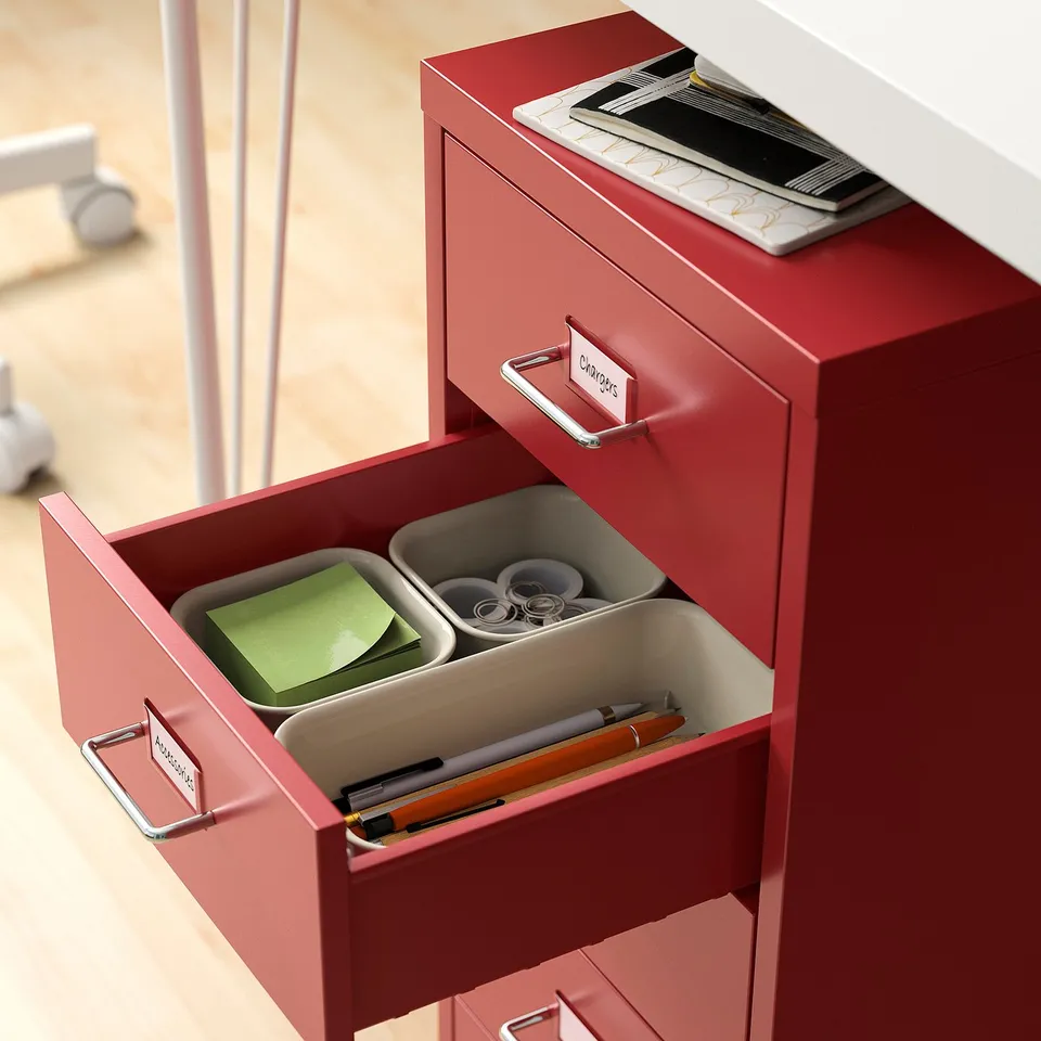 Red filing cabinet with drawers open, revealing office supplies organised in compartments.