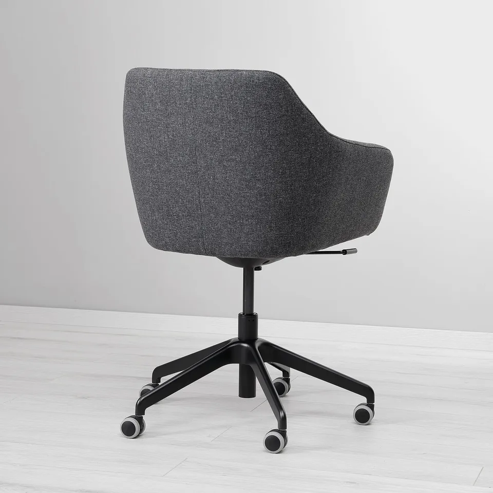 Modern grey office chair with padded seat and back, five-star base, and wheels, positioned on a wooden floor against a light wall.