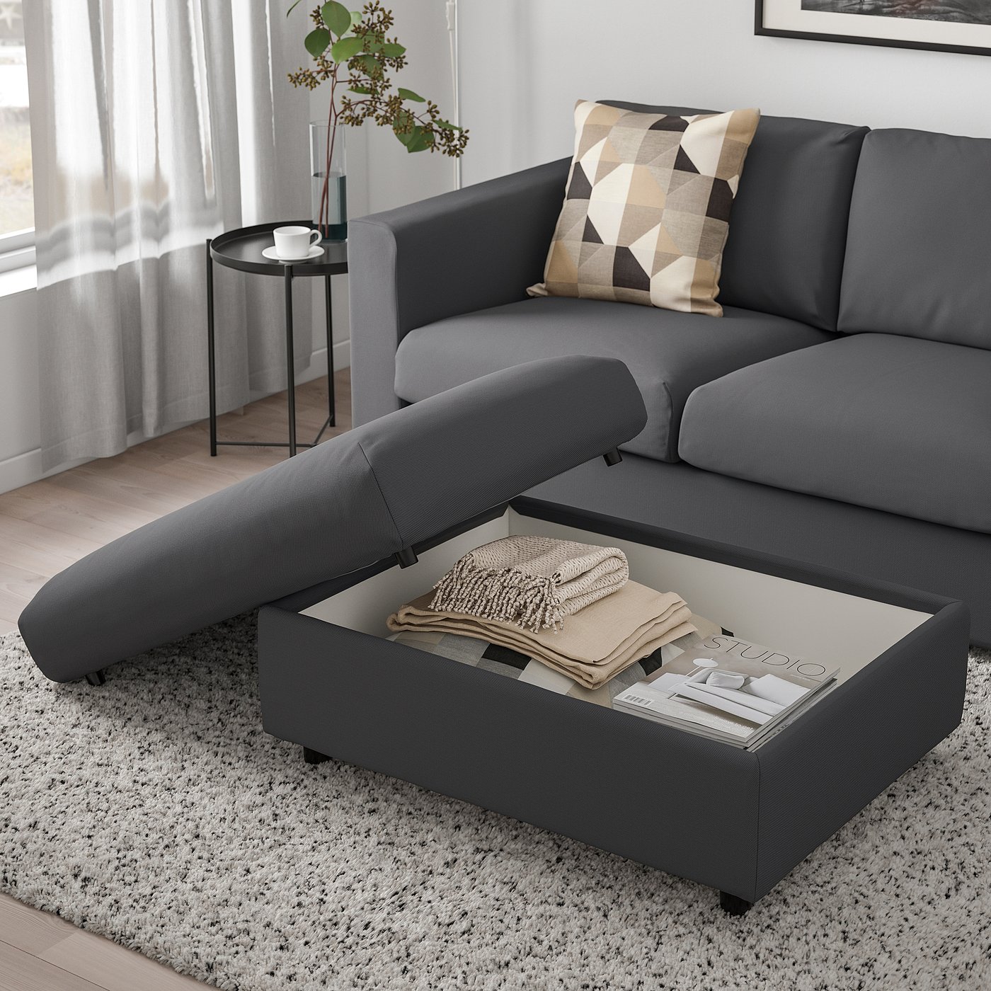 Modern living room with grey VIMLE sectional sofa, featuring a footstool with open storage compartment filled with blankets and a magazine.