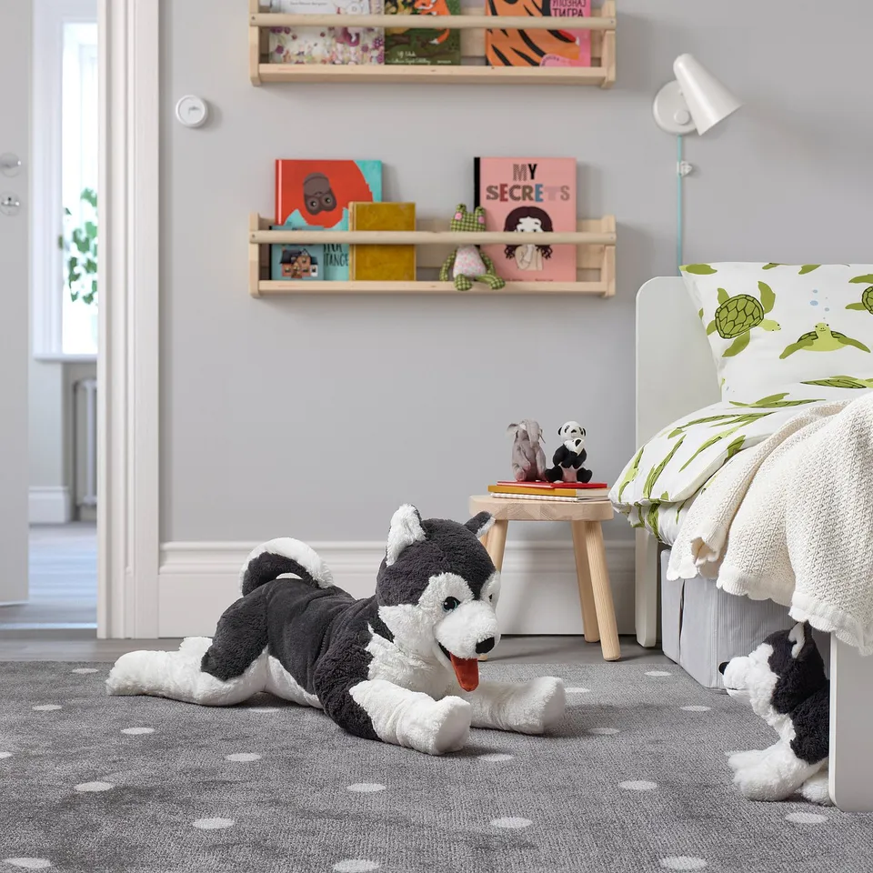 Grey/white stuffed husky on rug in kids room. Bookshelves, turtle chair, toys nearby.