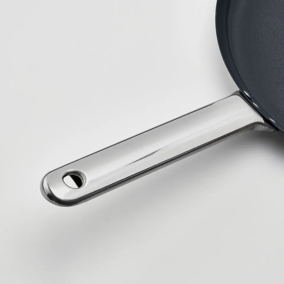 Stainless steel pan handle with hole, reflecting light, mounted on grey base, indicating quality and durability.