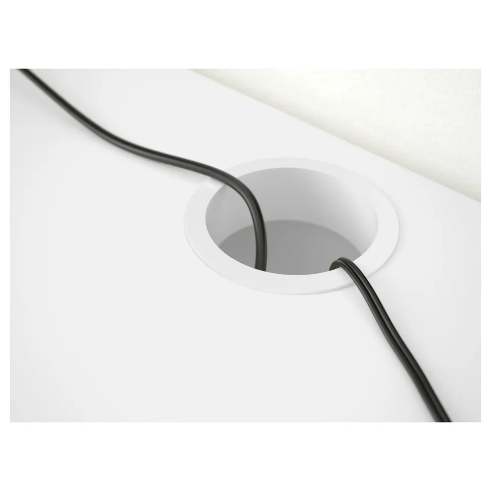 Cable management hole in SMÅGÖRA desk. Black cord passes through white circular cutout.