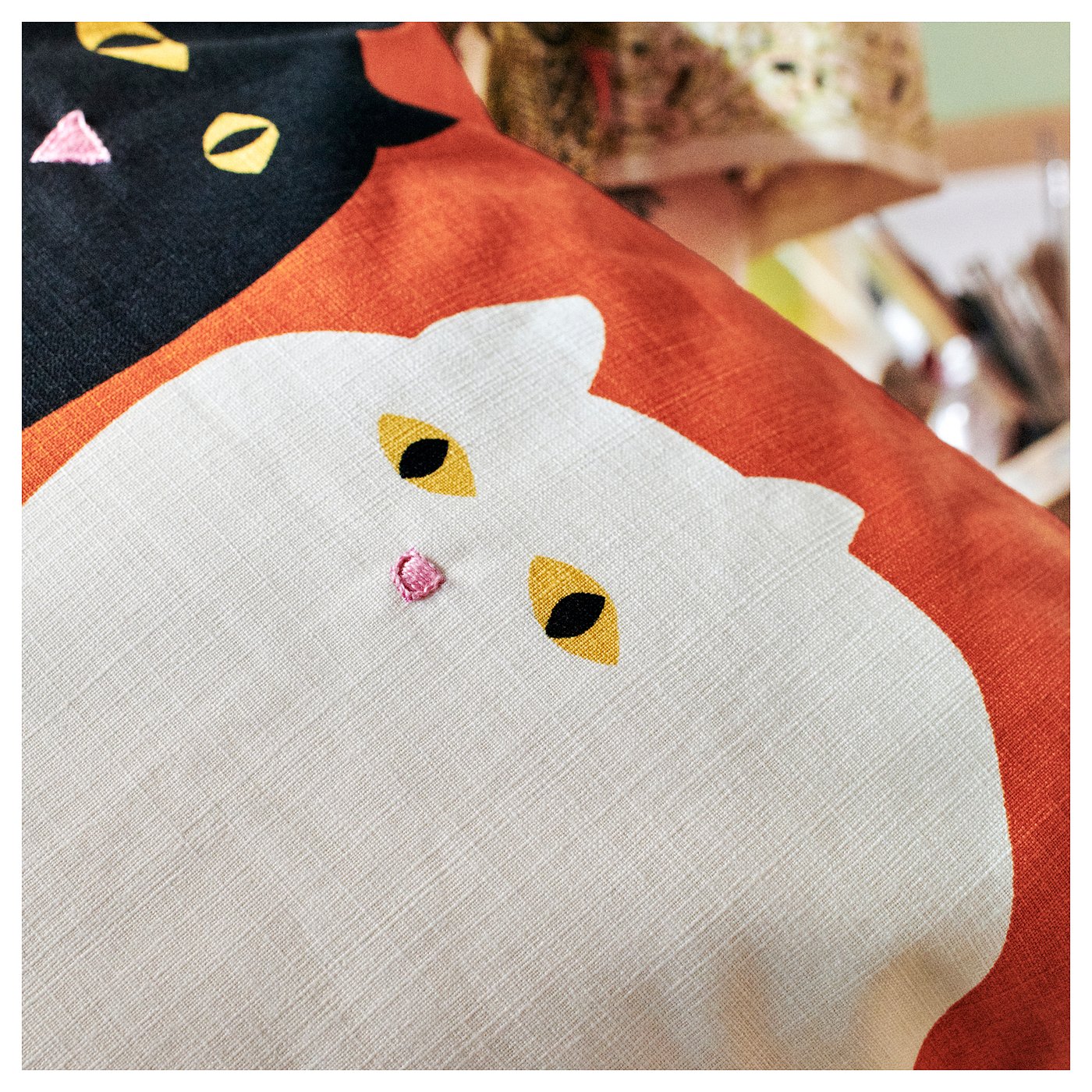 Adorable cat cushion, red, white, yellow. Hand-embroidered, cotton. Rounded design, playful cat face.