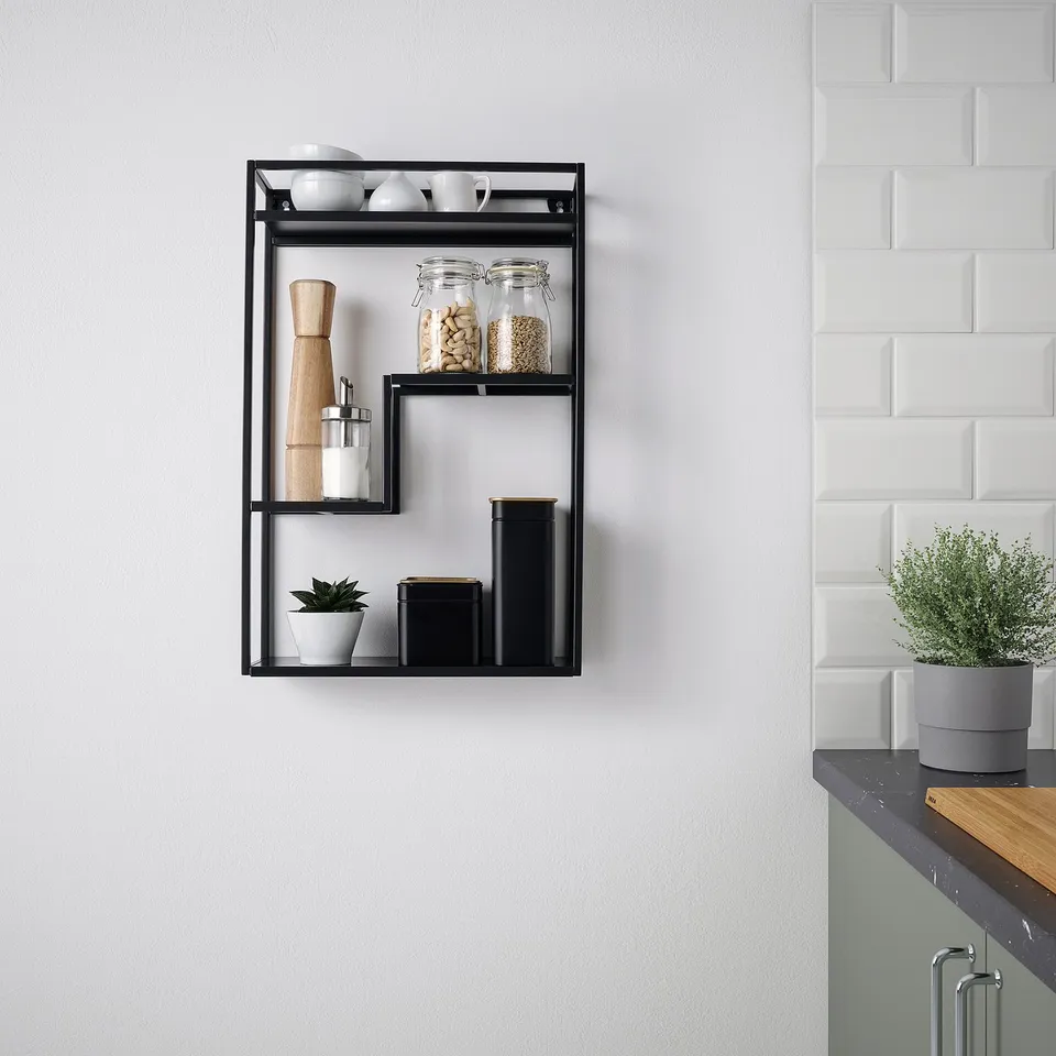 Black shelf with jars, containers, and a plant against a white wall.