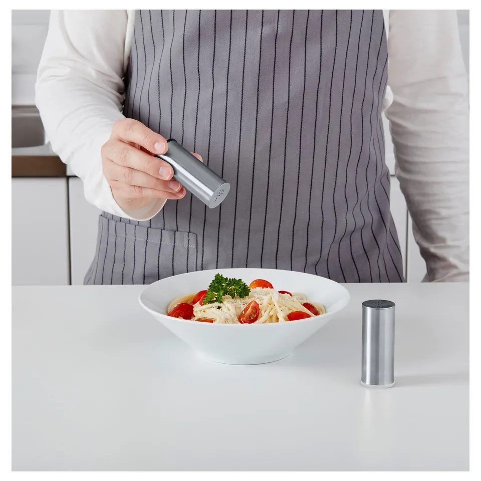 Person seasoning pasta dish with grinder. Bowl and grinder on white table.
