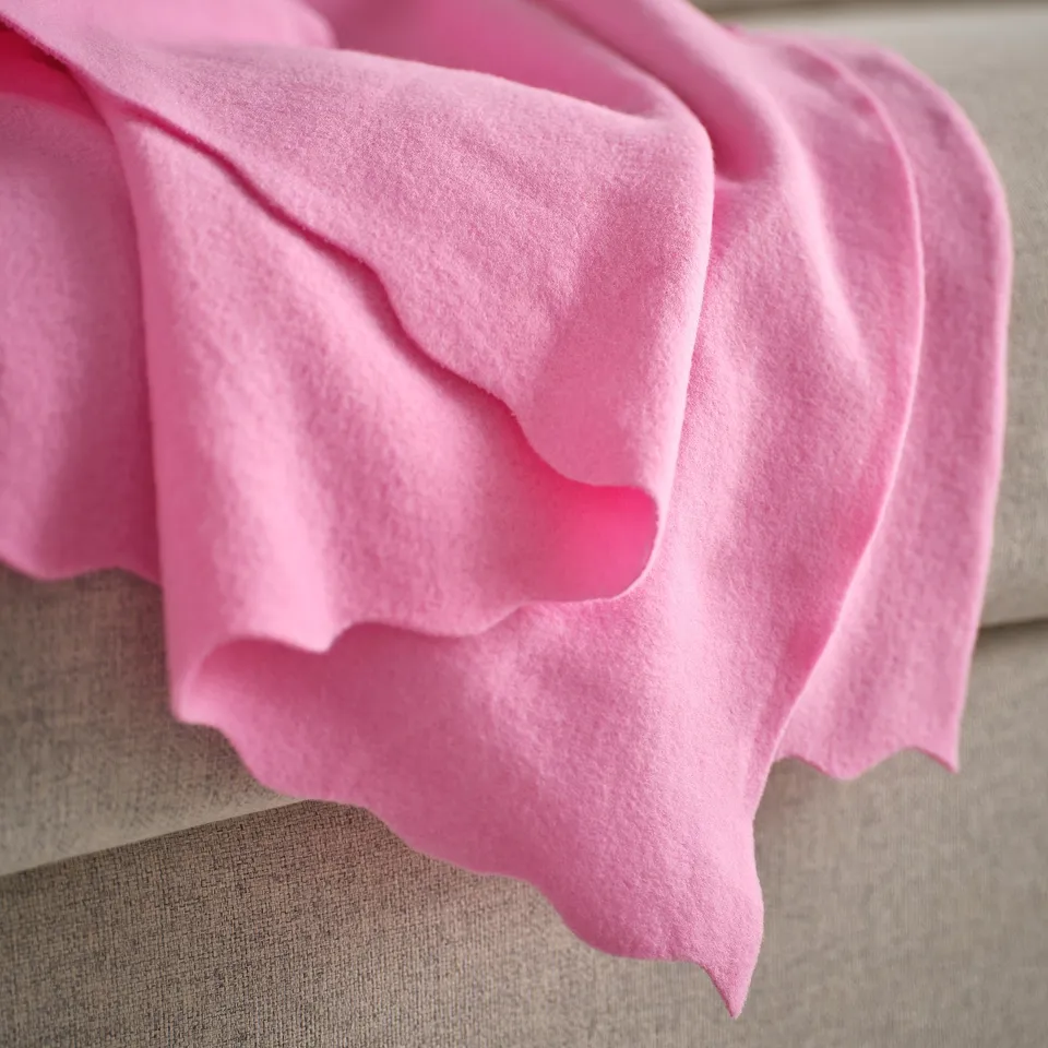 Bright pink, soft fleece blanket draped over a beige couch, showcasing its plush, cosy texture.