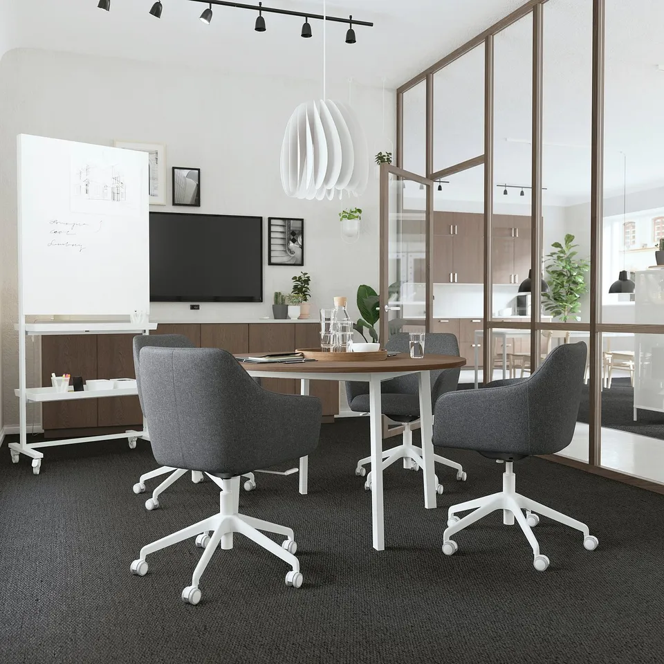 Modern office with grey swivel chairs, wooden table, tv, whiteboard, bright lighting, and glass partitions.