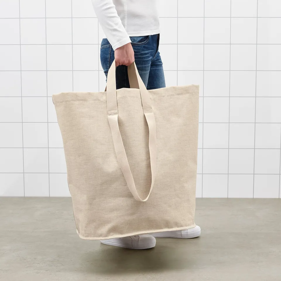 Person holding a large beige tote bag with handles, perfect for laundry.