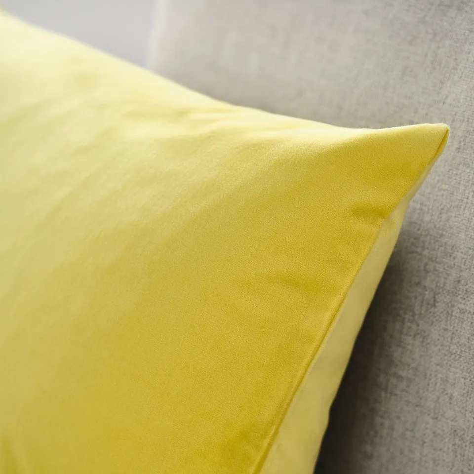 Close-up of a yellow velvety cushion on a soft grey surface. The texture and fabric quality look luxurious and inviting.