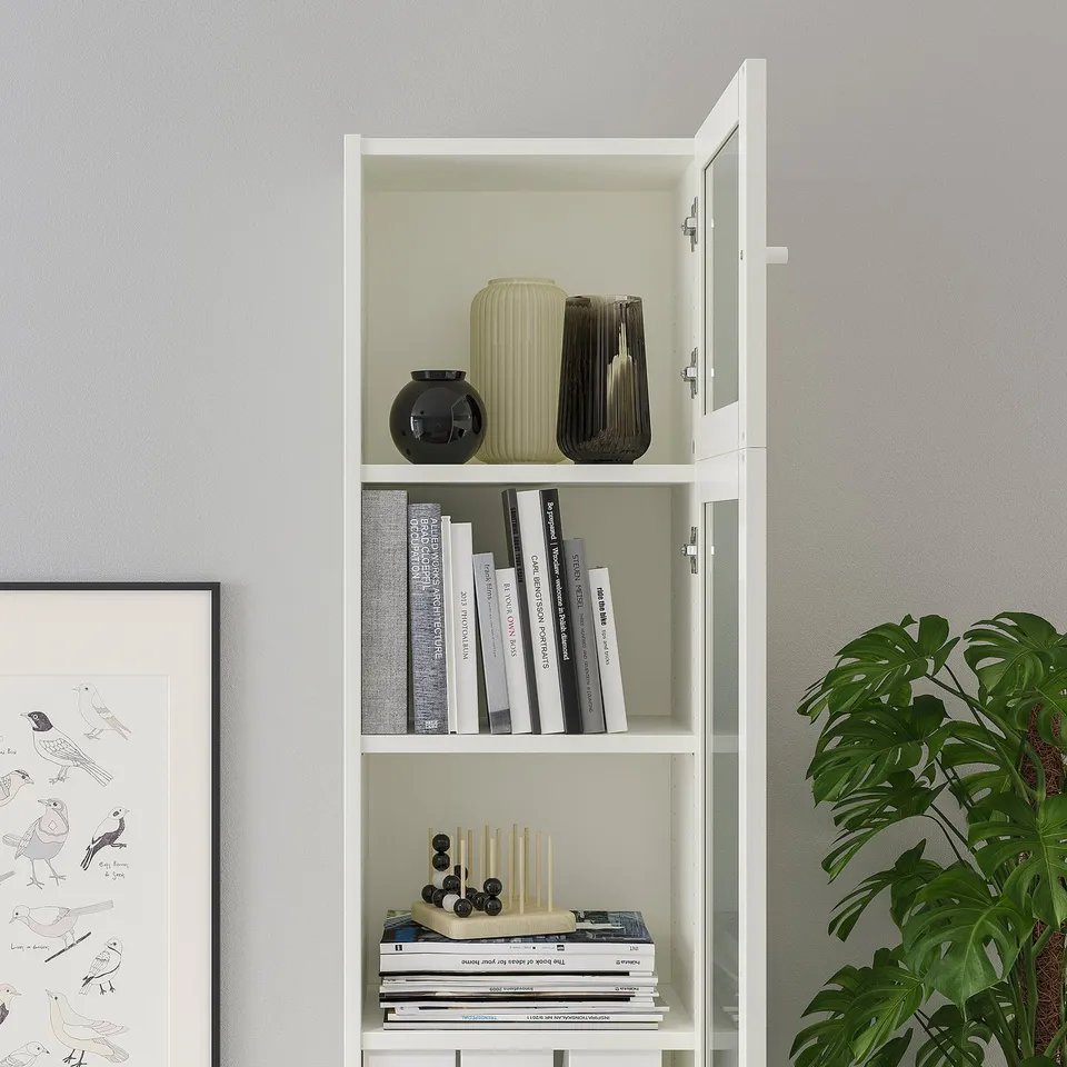 White BILLY bookcase with glass doors showcasing vases and books, utilising ceiling height and providing dust-free display.