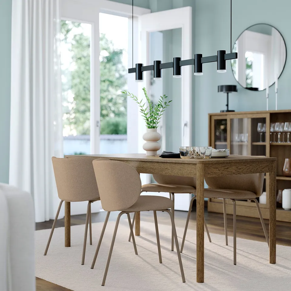 Modern grey dining set with square table, four fabric chairs, under sleek black pendant light; positioned near a window and wooden sideboard.