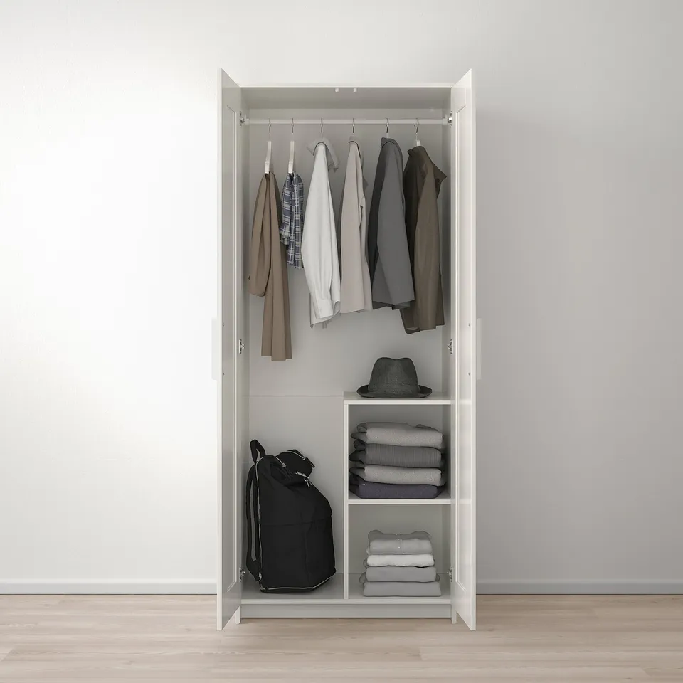 A BRIMNES wardrobe, storing folded clothes on shelves and hanging garments on rails, anchored to the wall for safety.