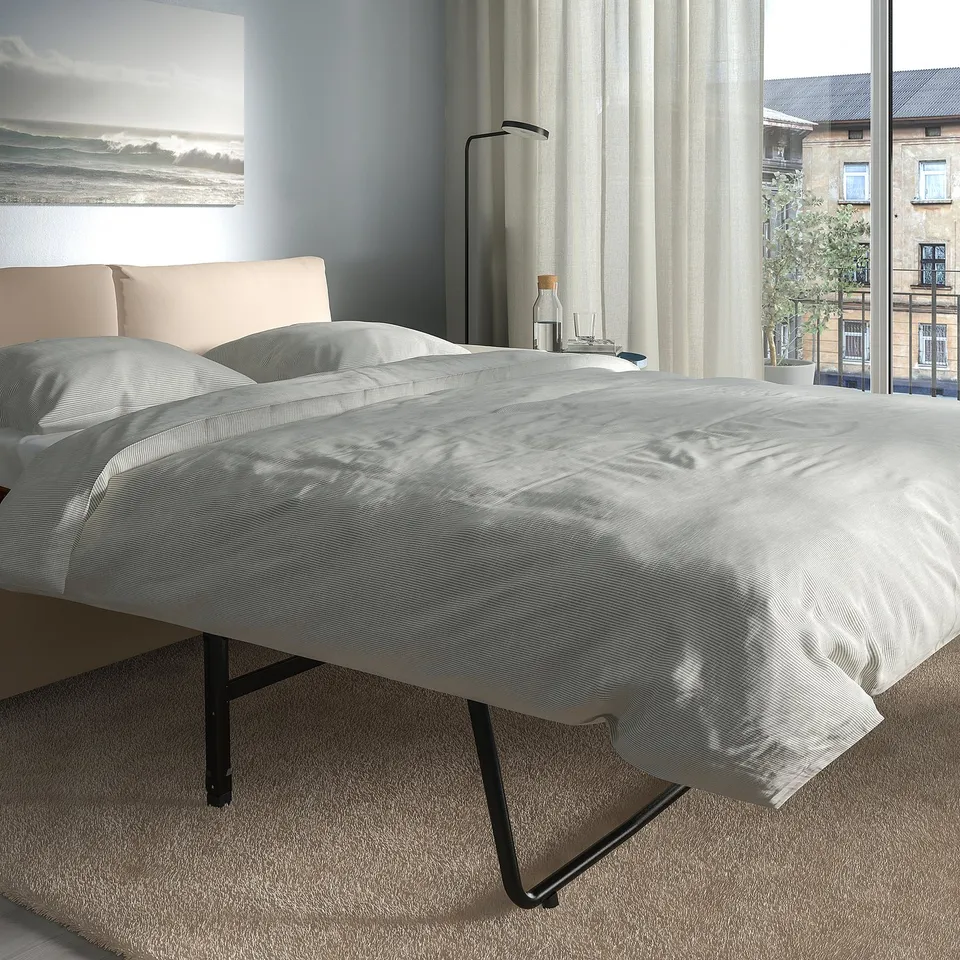 Modern sofa-bed with thick mattress, positioned near large window with curtains, showcasing comfortable and easily convertible design.