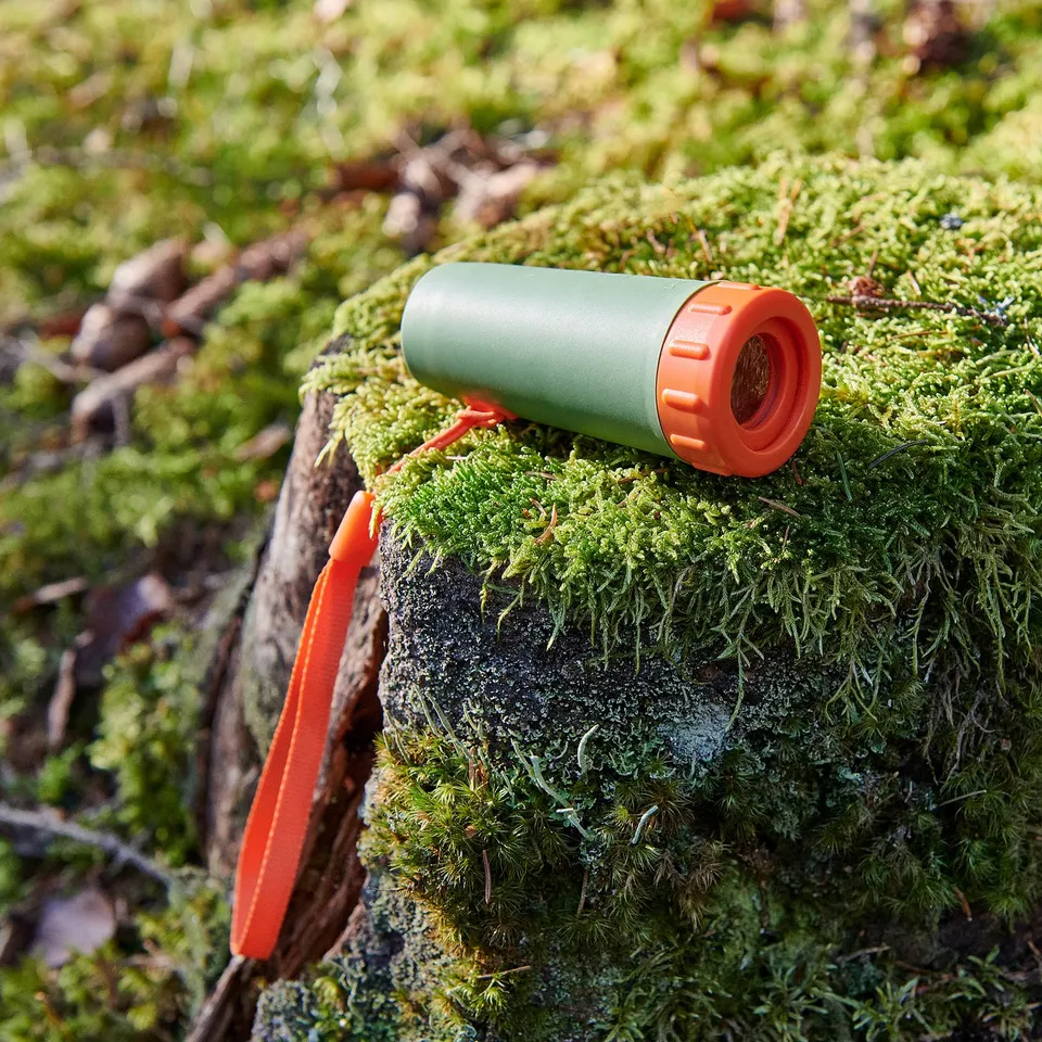 Small green binoculars with orange strap and details on mossy log.