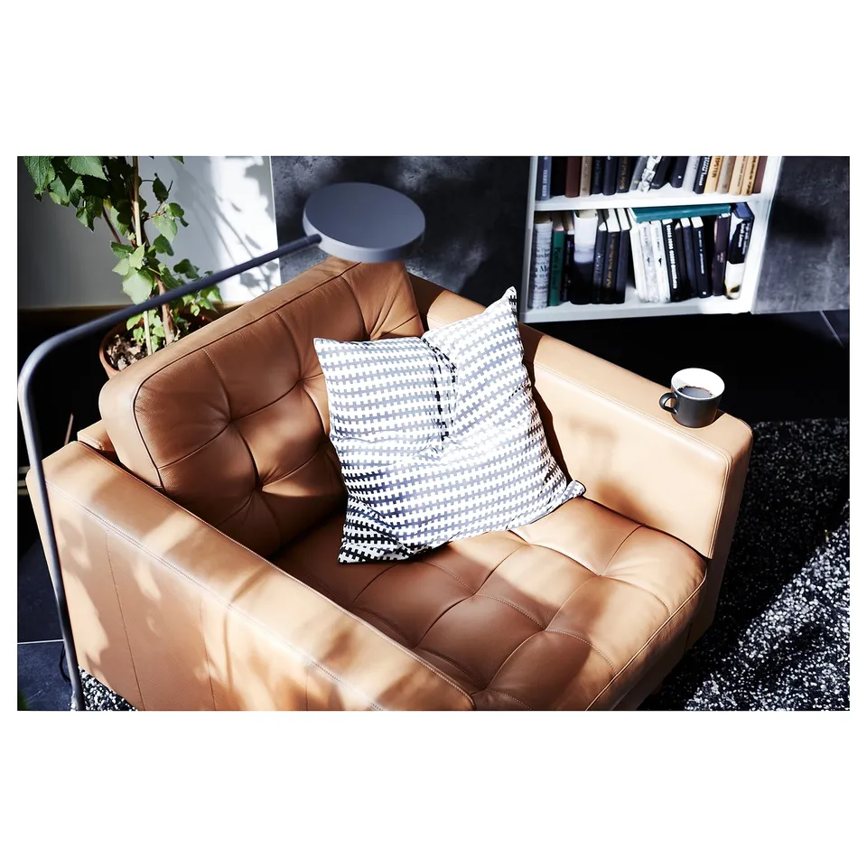 Modern living room with tan leather armchair, geometric pillow, mug, plant, and bookshelf.