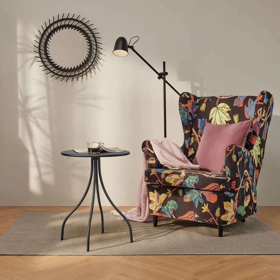 Modern living room with round mirror, tall lamp, floral armchair, side table with tea and magazine.