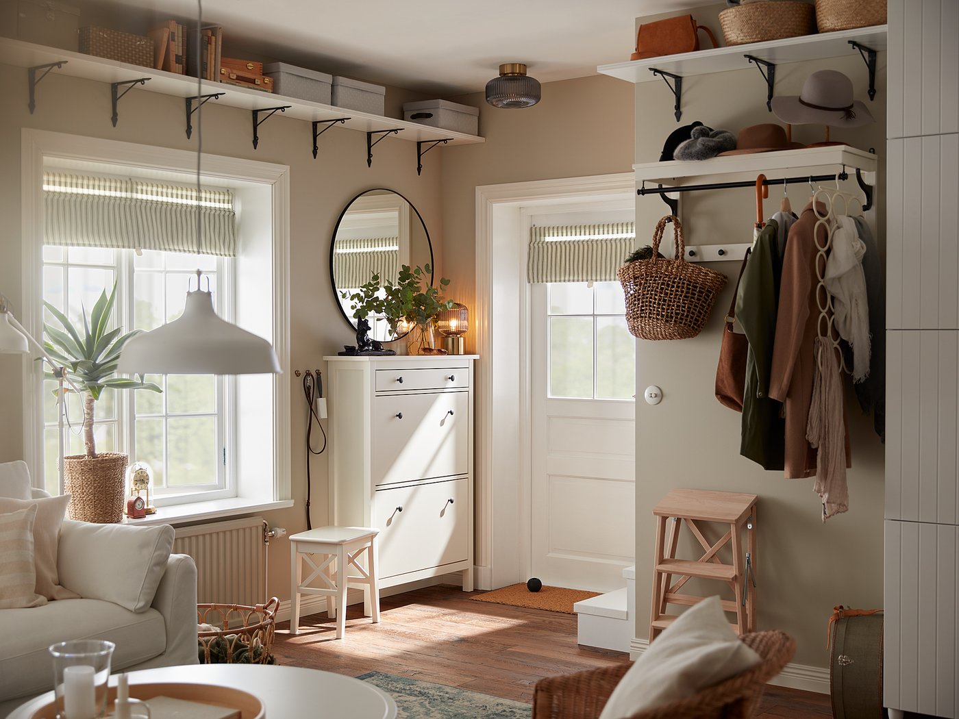 Modern living room with wooden floors, beige walls, and natural light. White furniture and plant decor.