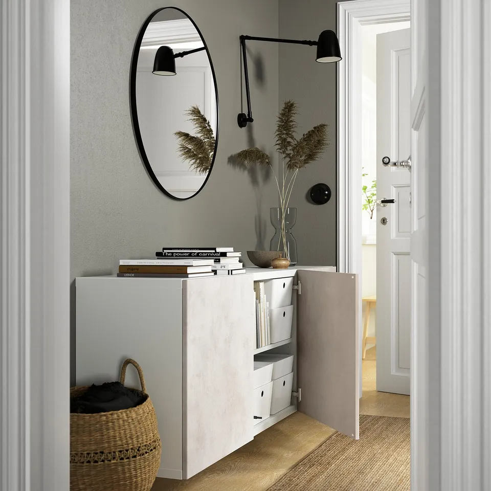 Entryway with BESTÅ cabinet, open door exposing shelves, above it, a round mirror and two lamps, one on each side.