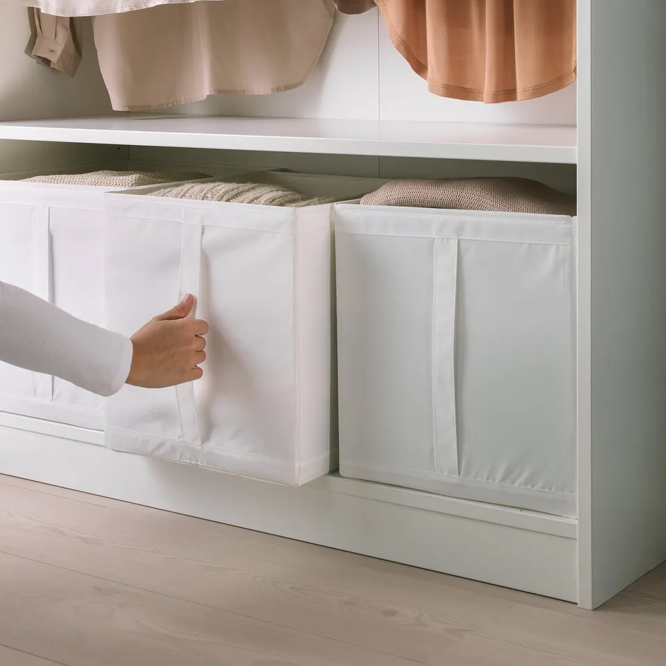 Person pulling out white SKUBB storage box from wardrobe, showcasing handle and compact design.