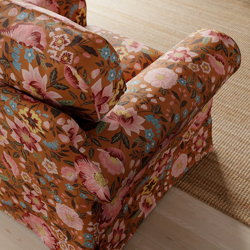 Floral-patterned armchair with rolled arms on a woven beige rug. Soft, supportive cushions, vibrant flowers against earthy brown backdrop.