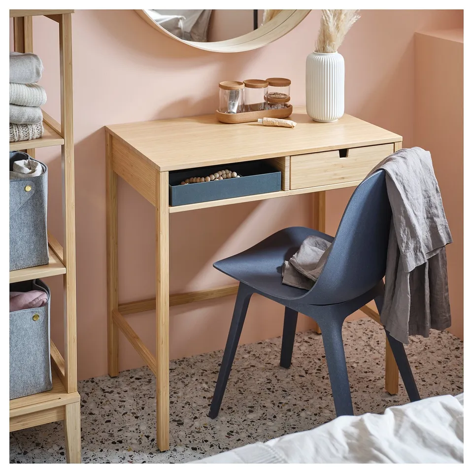 A NORDKISA wooden desk with a blue drawer, paired with a blue chair. Its set against a pink wall.