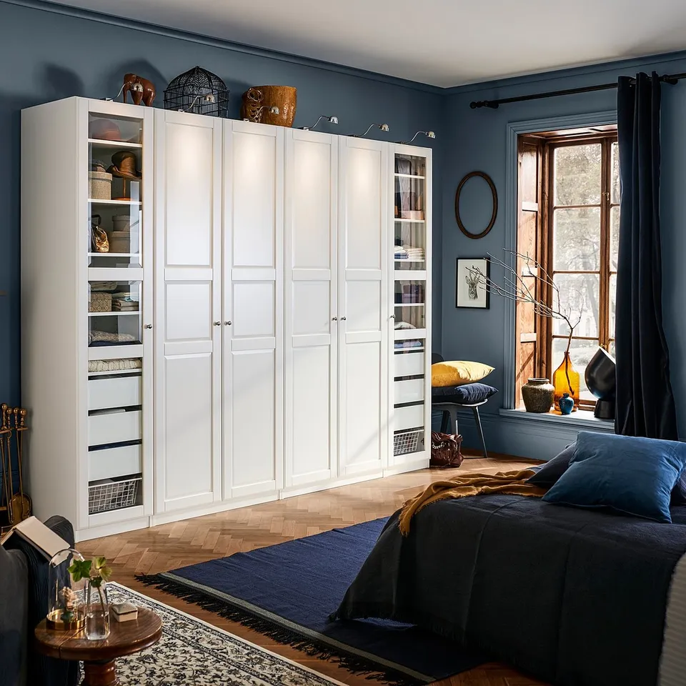Large white TYSSEDAL wardrobe with glass panels displays decor. Blue walls and dark furniture in a cosy room.