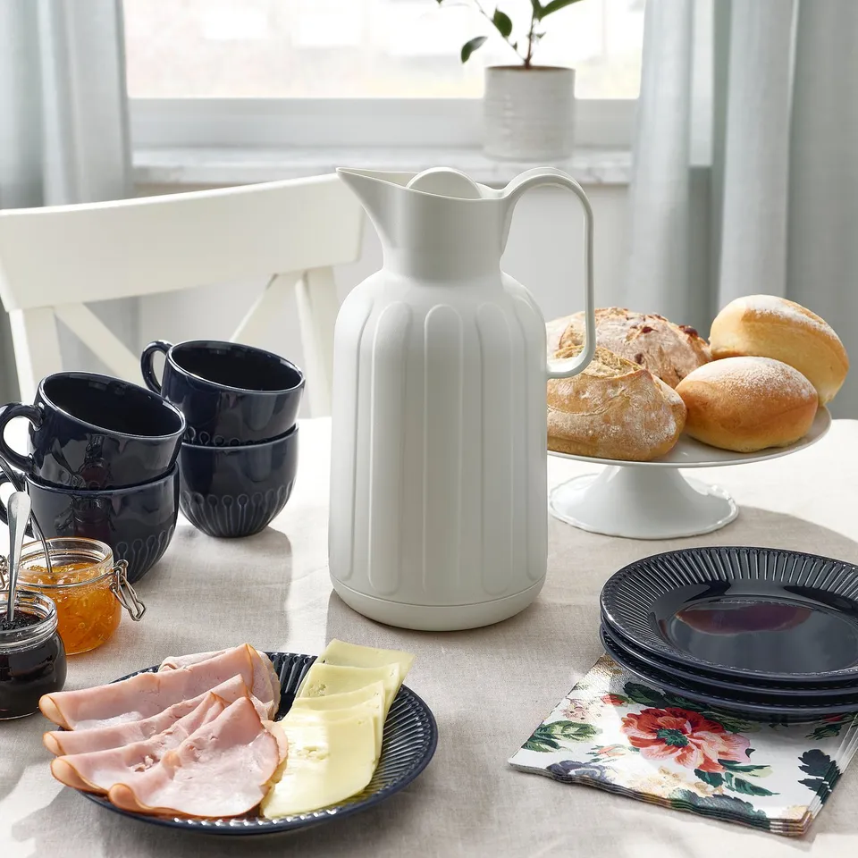 Table setup with TAGGÖGA flask, mugs, pastries, cheeses, jams, and plates, ready for a cosy fika.