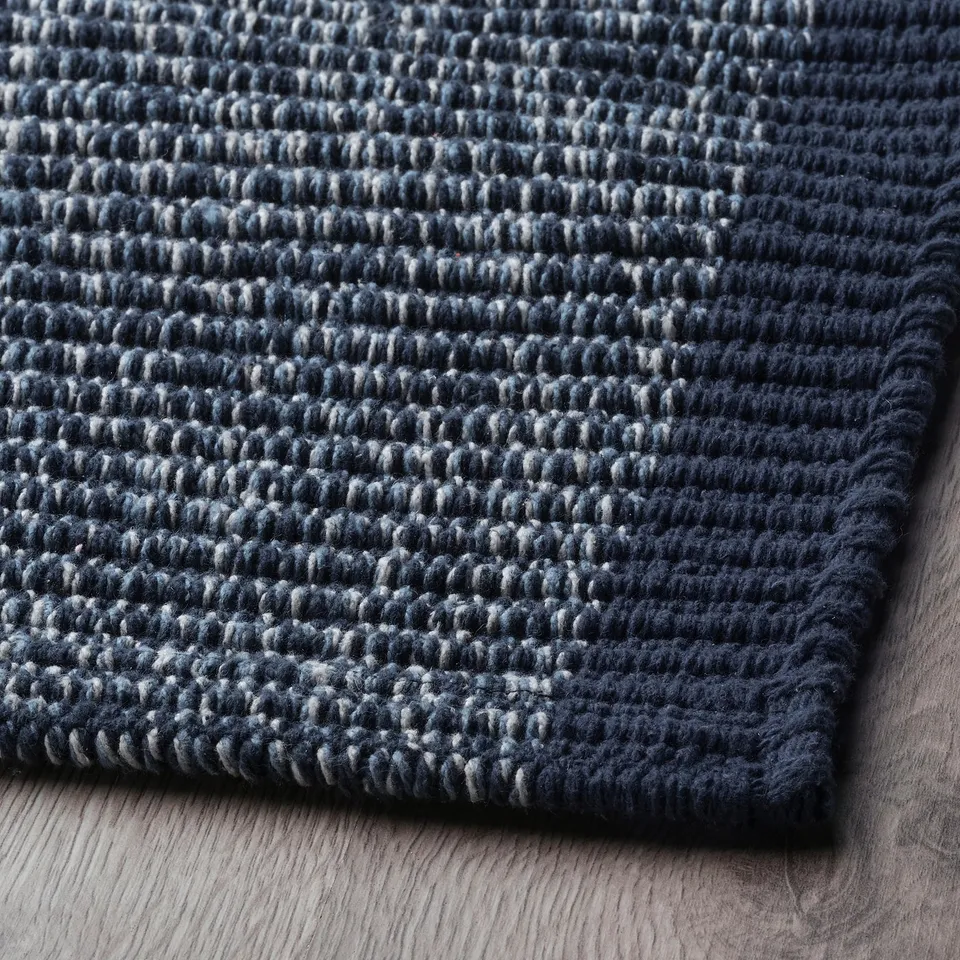Dark blue textured cotton rug, folded on wooden floor. Soft, high-quality material, neatly stitched edges.