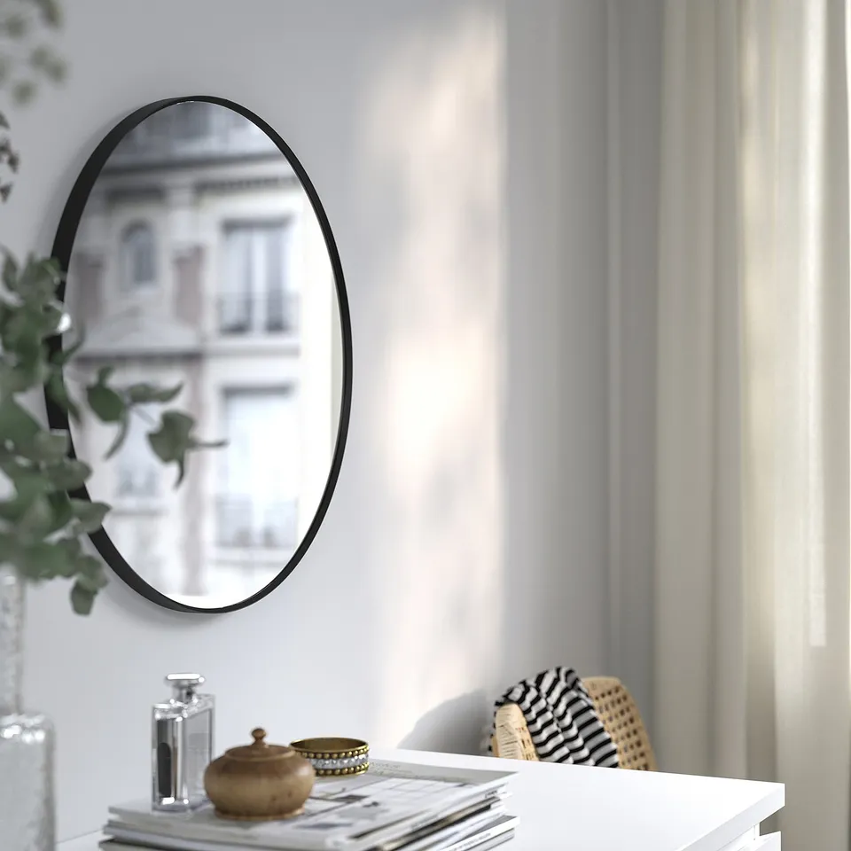 Round black-framed mirror on wall reflects building, placed above table with decor.