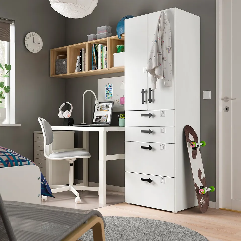 Modern kids room with SMÅSTAD white wardrobe and desk. Includes chair, laptop, bookshelf with books, and skateboard.