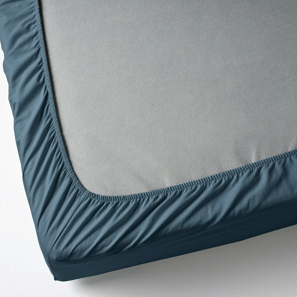 Corner of grey mattress with blue fitted sheet.