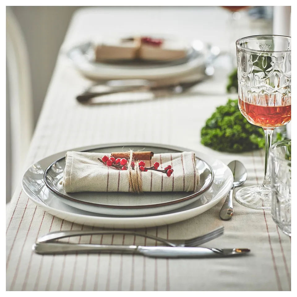 Elegant table setting with white plates, striped napkins, and wine glass, arranged neatly on a white tablecloth.