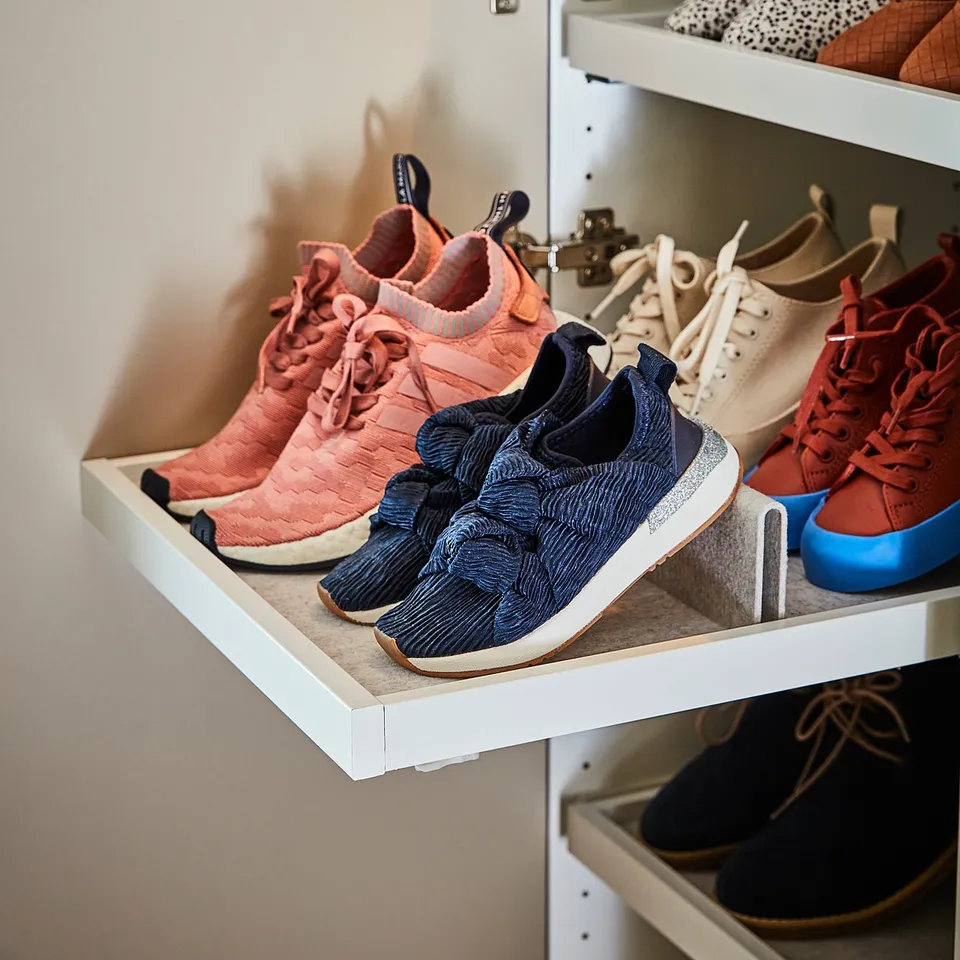 Shoe rack with colourful trainers, including peach, blue, white, and red pairs, neatly organised in white shelves.