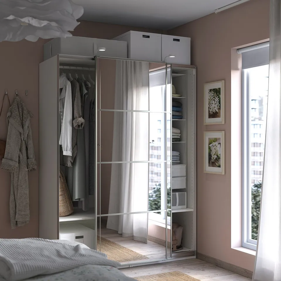 Modern bedroom with grey PAX wardrobe featuring mirrored doors, neatly organised clothes and city view.