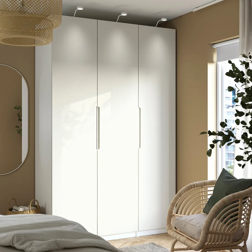 Large white TONSTAD wardrobe with three sections next to a window. A wicker chair with a green pillow is beside it.